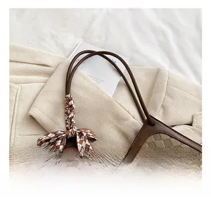 Detail of woven tote bag featuring brown leather trim and a plaid bow on the handle