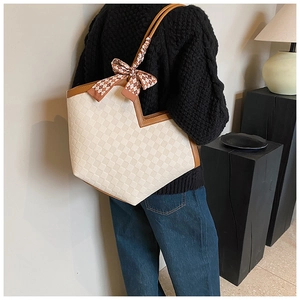 Detail of large tote bag showing cream checkered texture and brown leather trim
