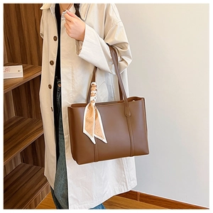 Detail of a brown leather tote bag with a decorative beige printed silk scarf tied on handle