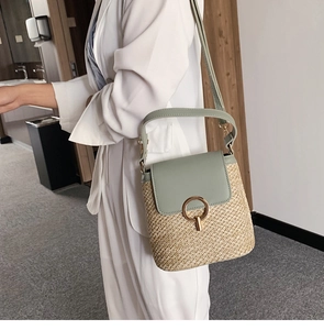 Détail du sac seau en paille tressée avec rabat en cuir vert et fermoir rotatif doré