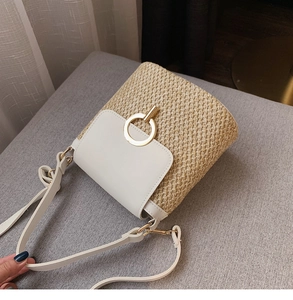 Détail du sac seau en paille tressée avec rabat en cuir blanc et boucle dorée
