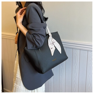 Close-up of black litchi pattern tote bag featuring decorative silk scarf and gold lettering