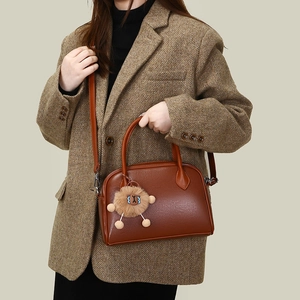 Detail of caramel leather Boston bag featuring a cute plush lion charm and top handle