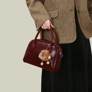 Detail of dark burgundy vintage boston handbag with a cute plush lion charm accessory