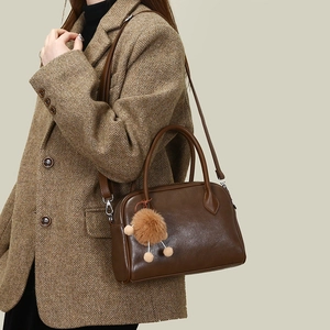 Detailed view of brown faux leather boston bag styled with a wool blazer and plush charm
