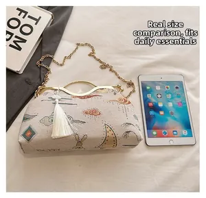 Detailed view of beige embroidered shell bag with gold handle and tassel on a desk