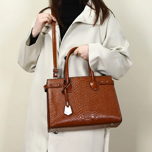 Detail of a brown crocodile pattern tote bag with top handles and adjustable strap