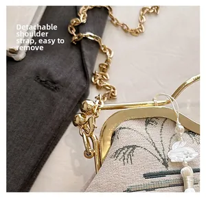 Detail of detachable gold chain strap and vintage embroidery on beige shell bag