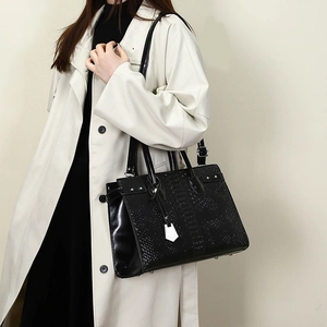 Close-up of black crocodile-embossed leather tote with metallic stud detail and white tag