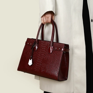 Detail of burgundy crocodile pattern handbag with silver hardware and dual handles