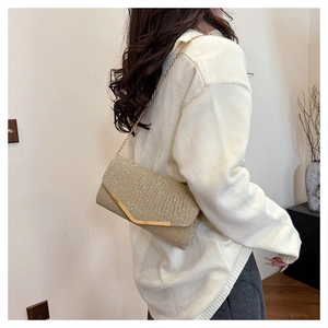 Detail view of a gold glitter envelope evening clutch with V-shaped metal trim and chain