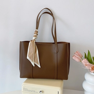 Dark brown leather tote bag with decorative fashion scarf on a cream-colored vintage drawer