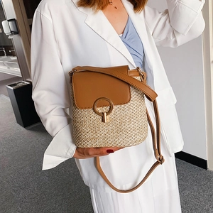 Sac seau en paille avec rabat en cuir marron et boucle dorée porté par mannequin