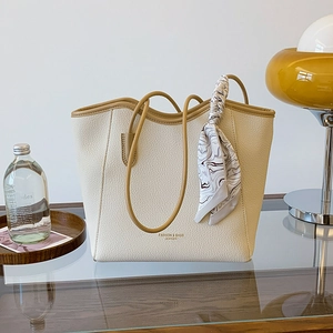 Minimalist beige leather tote bag with brown trim and silk scarf on a wooden table