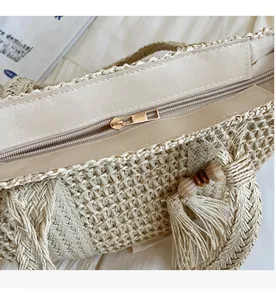 Detail of a beige woven straw bag featuring a smooth metal zipper and decorative tassels