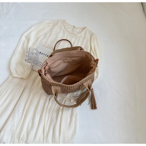 Detail of straw tote bag interior lining with zip pocket and boho tassel charm