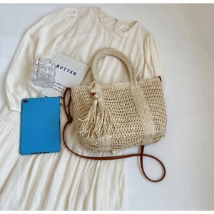 Detail of straw woven tote with fringe tassel and brown strap on a vacation outfit