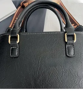 Close-up of black lychee texture leather tote with golden logo and woven strap