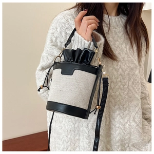 Detail of canvas bucket bag with leather trim and gold metal hooks on a white sweater