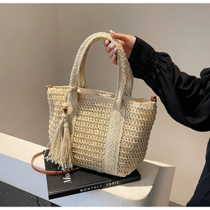 Close-up of woven straw tote bag with tassel charm and slim leather strap on magazines