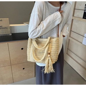 Detailed close-up of straw woven tote bag featuring long tassels and crossbody strap