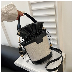 Detail of beige woven bucket bag with black leather trim and polished gold hardware