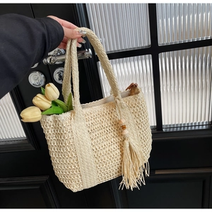 Detail of hand-woven straw tote with bohemian tassel and yellow tulips