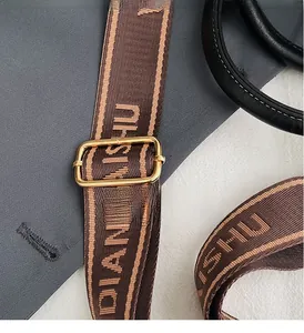 Detail of adjustable woven shoulder strap with gold buckle and letter jacquard pattern