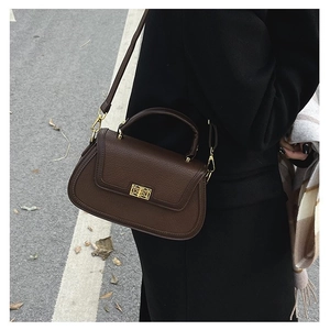 Détail d'un sac à main marron à motif litchi avec boucle dorée dans un décor de rue