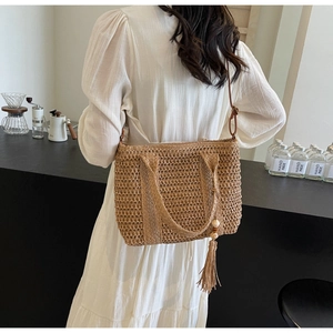 Detail of hand-woven straw bag with long strap and wooden bead tassel in casual setting