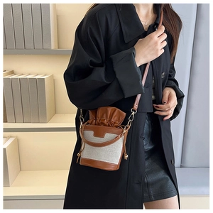 Detailed close-up of a canvas and leather bucket bag worn as a crossbody shoulder bag