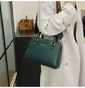 Detail of dark green tote bag with wide logo strap and gold hardware on white coat