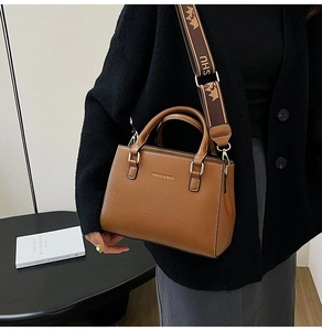 Caramel tote bag with wide logo strap shown on a model in a minimalist setting