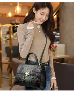 Detail of black crocodile pattern leather handbag with gold clasp on a beige sweater