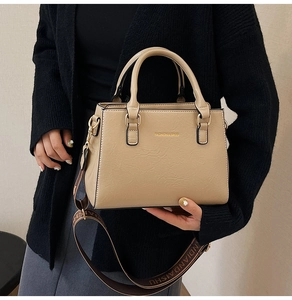 Detail of beige textured leather tote with wide woven strap and gold fashion lettering