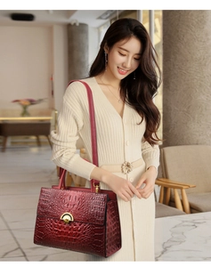 Detail of burgundy crocodile-embossed handbag with gold clasp and top handle style
