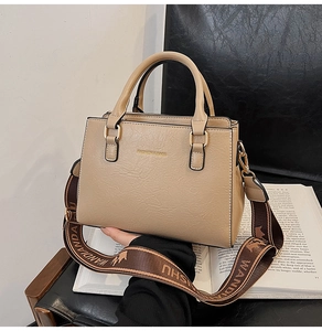 Detail of light brown tote bag with wide embroidered strap on an open book