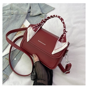 Detail of burgundy leather crossbody bag featuring silk scarf handle and logo print
