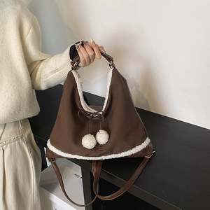 Détail de la bordure en fausse fourrure et des pompons blancs sur un sac marron