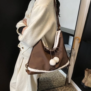 Détail d'un sac à bandoulière marron orné de fourrure synthétique et de pompons en peluche
