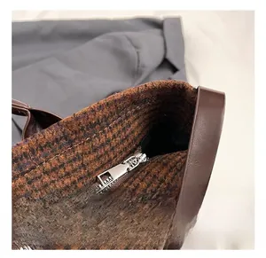 Detail view of silver metal zipper and brown plaid tweed material on the tote bag