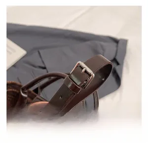 Detail of adjustable dark brown leather strap with polished silver metal buckle on tote bag