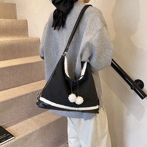 Détail du sac fourre-tout noir avec garniture en fausse fourrure blanche et pompons
