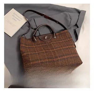 Detailed view of checkered tote bag with leather handles on grey suit background