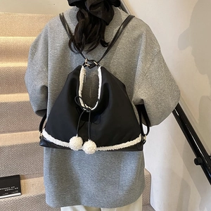 Détail d'un sac à dos en nylon noir avec bordure en fausse fourrure blanche et pompons