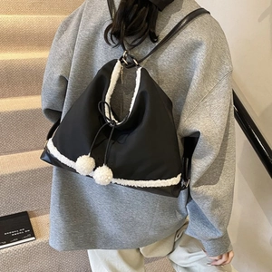 Détail d'un sac à dos noir avec bordure en peluche blanche et pompons du cordon
