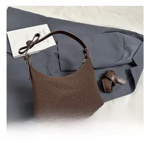 Dettaglio borsa hobo marrone con manico in pelle e fiocco su tessuto grigio