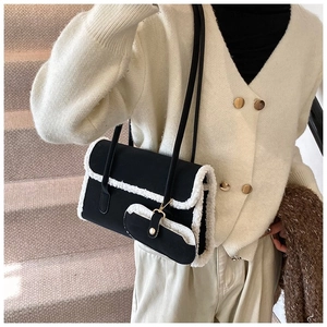 Detail of black shoulder bag featuring plush white faux fur trim and front pocket design