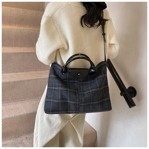 Detail of checkered tote bag showing polished black handles and textured wool pattern