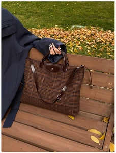 Close-up of brown quilted tote bag with leather flap and handle on autumn bench